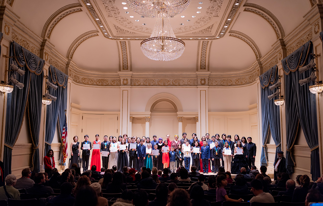 Members of the CPP Piano Ensemble and other participants stand on the Carnegie Hall stage. 