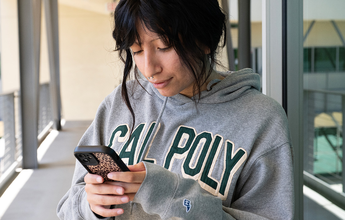 female student wearing a grey Cal Poly Pomona tshirt looks at her cell phone. 