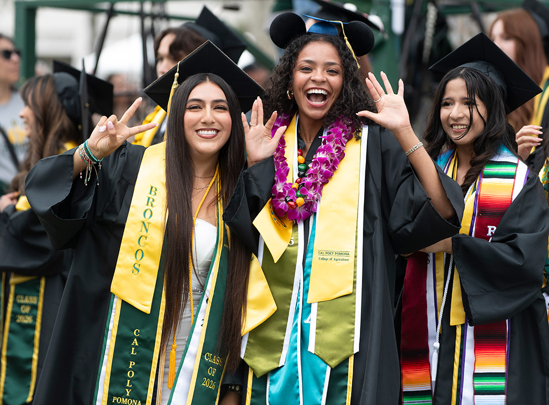 Two Female graduates smile, one wears a Disney Mickey Graduation Cap