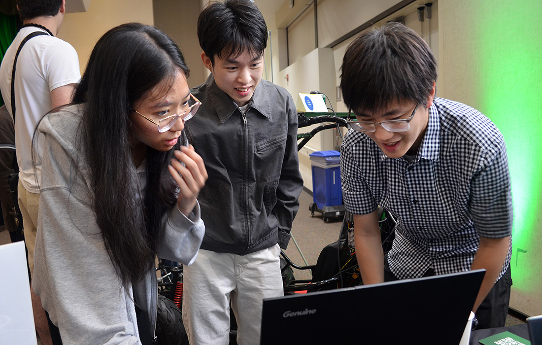 Three students, one female and two male look at a screen during the AI Fair and Hackathon