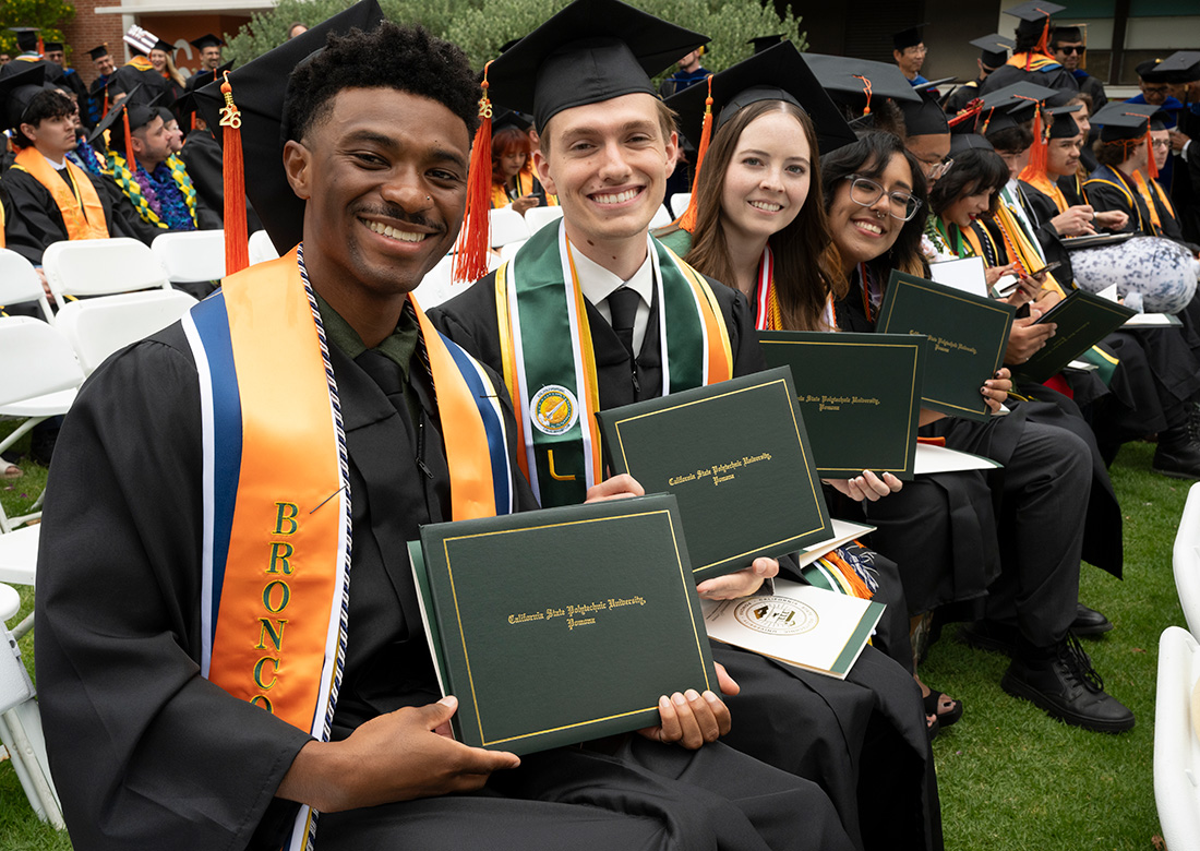 Graduates from the College of Engineering smile while holding their diplomas. 