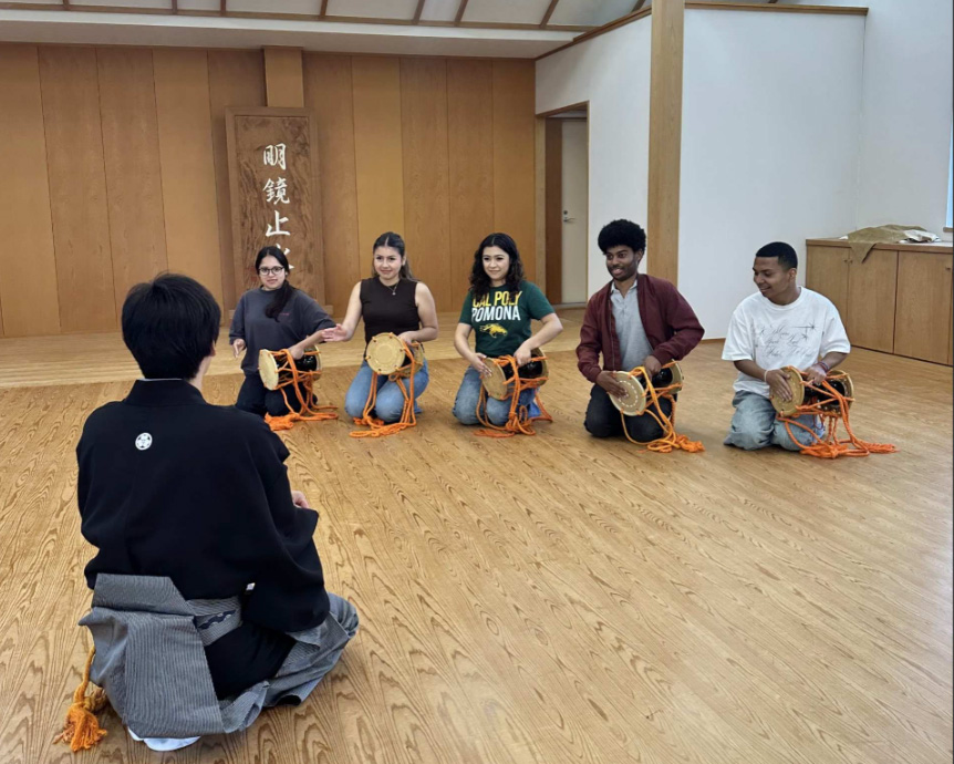 Students kneel in a room while learning how to play a Japanese instrument.