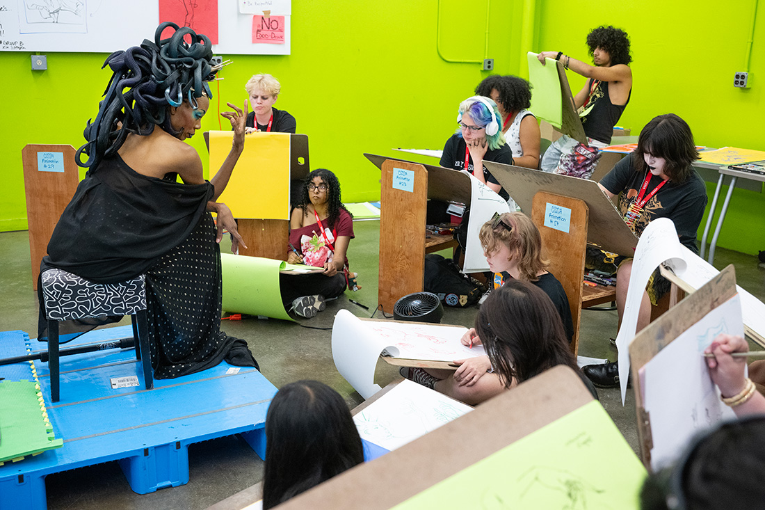 Students participate in a life drawing of a woman wearing a medusa head piece.