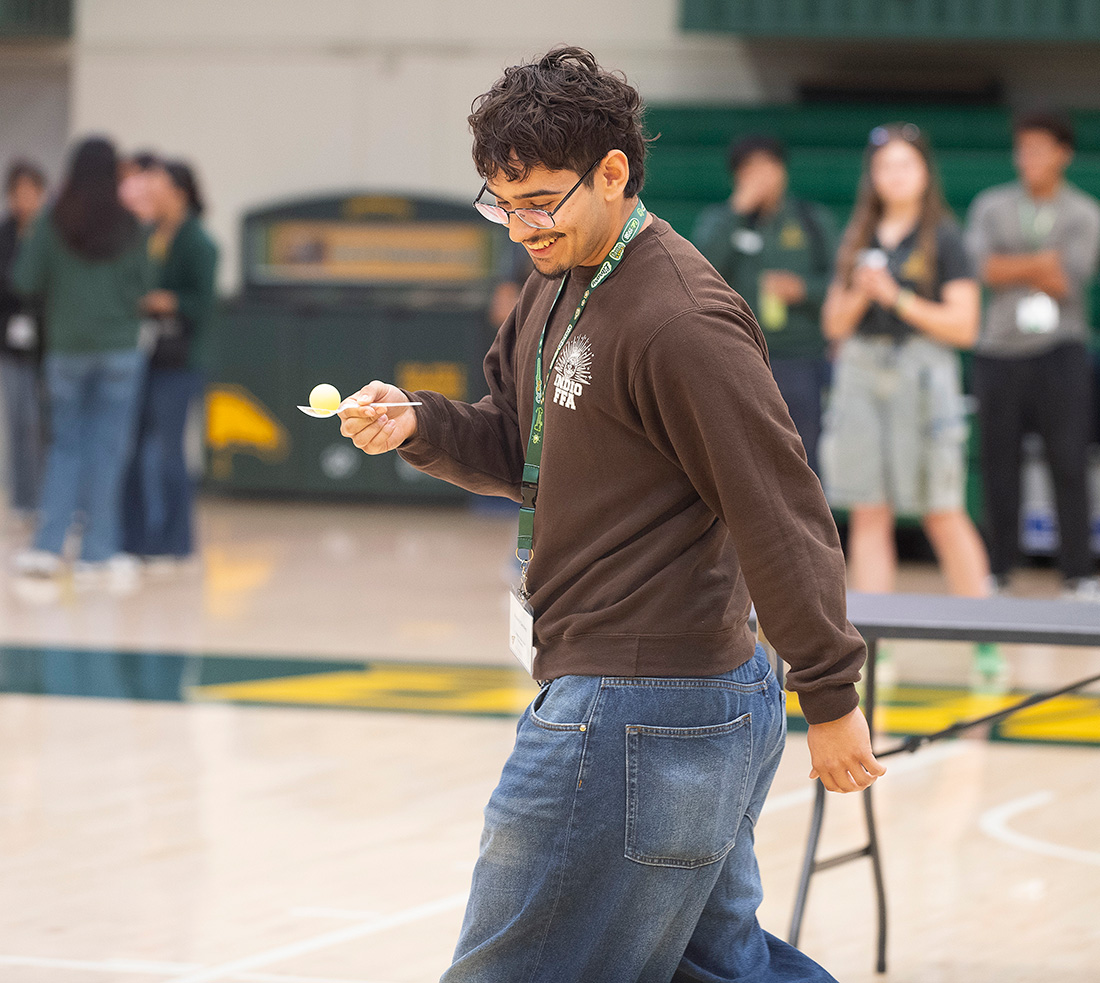A male student participates in a game walking across the gym holding an egg in a spoon