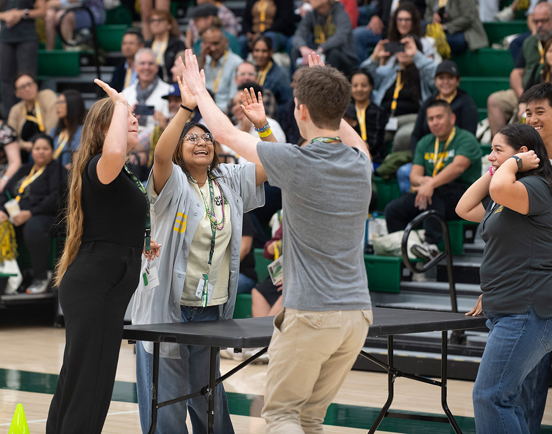 A team of three students high five each other during an orientation game