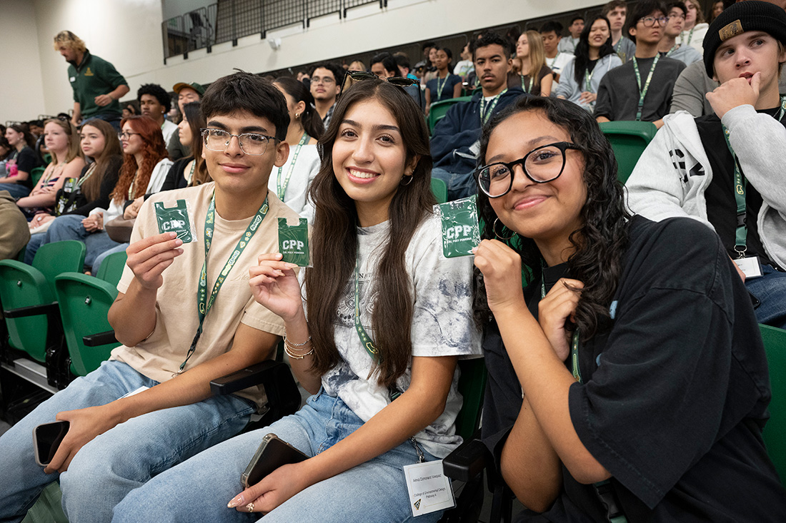 Three students hold up a CPP badge while sitting in the Kellogg Gym at orientation