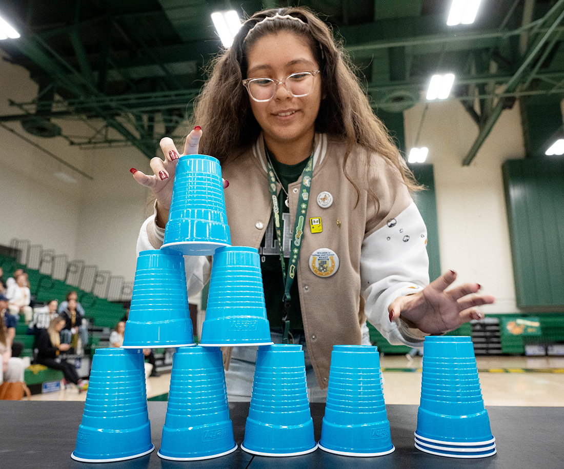 A female student plays a game stacking teal colored cups
