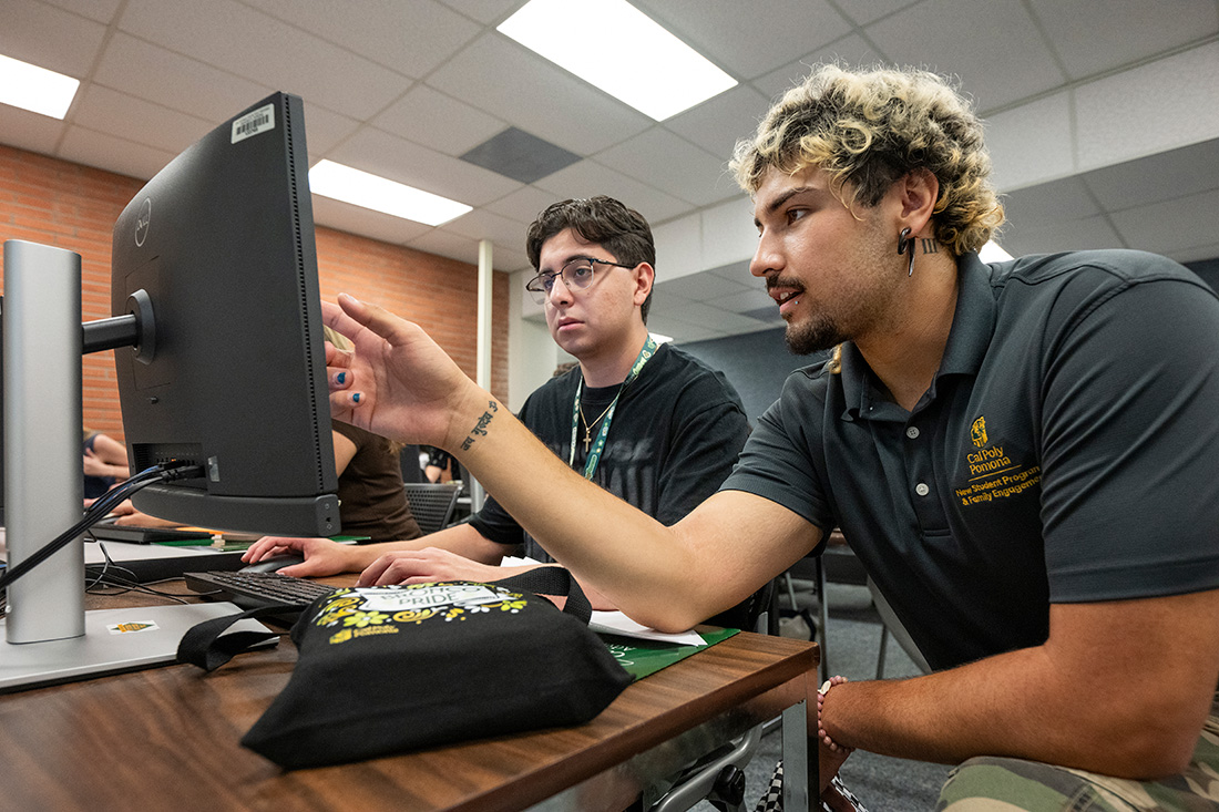 A male student works with a Cal Poly Pomona volunteer on a computer during orientation.