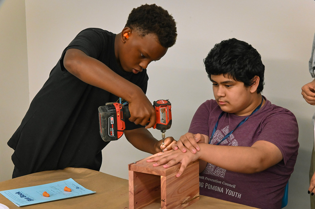 Two boys work with tools to create a wood box. 