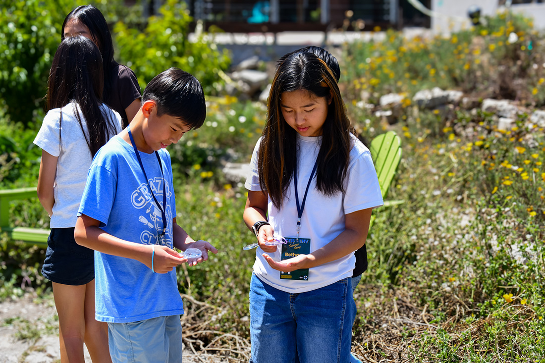 Two young students, male and female, look at objects through a magnifying glass.