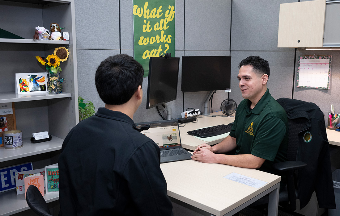 A male advisor and male student in conversation in an office.