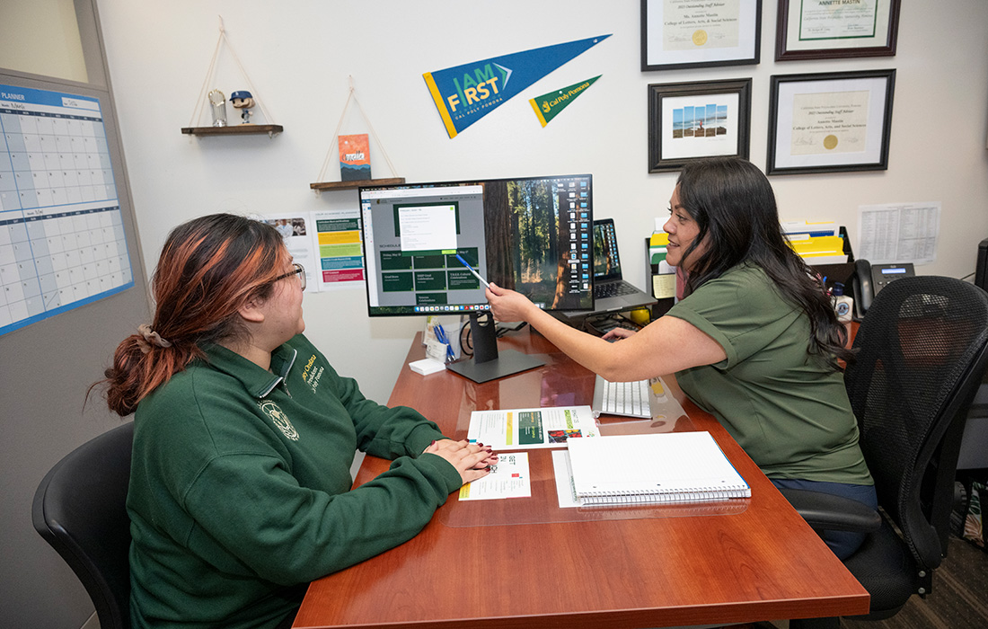 Female advisor shows a female student something on her computer. 