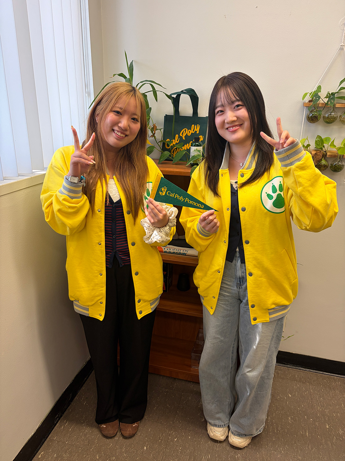 Two female japanese students smile while making a peace sign.