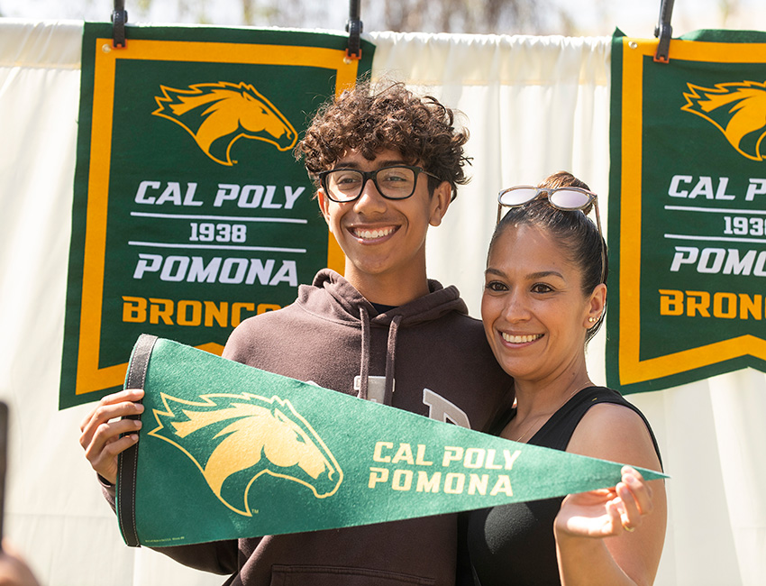A son and his mother pose for a photo holding a Bronco flag.
