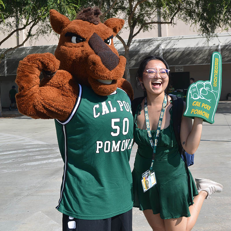 Female student holds foam finger and poses with Billy Bronco