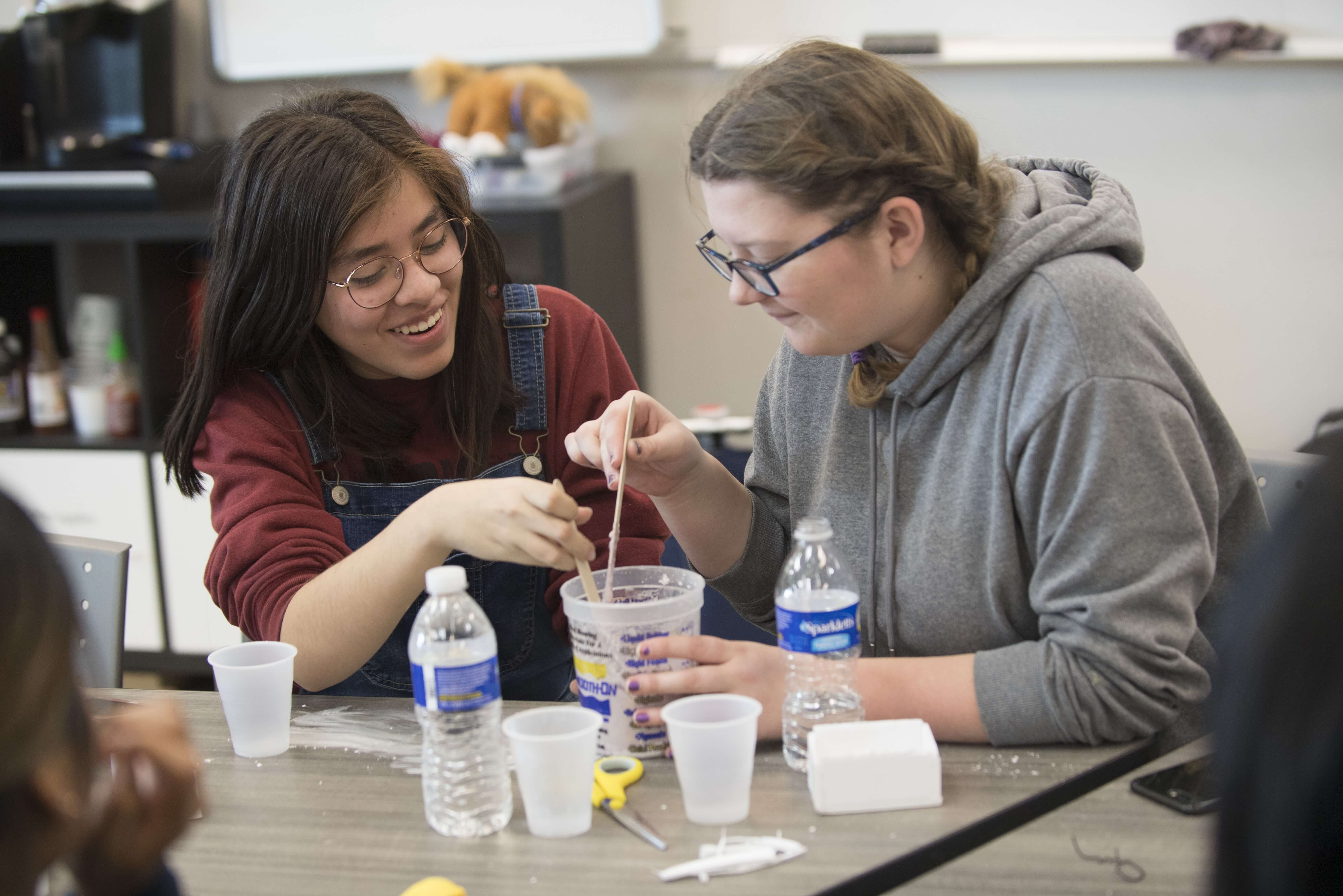 Two students sitting down and mixing an item in a cup