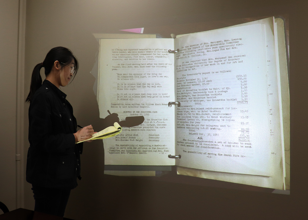 Image of Kelly Wong looking at a screen projection of a textbook and taking notes