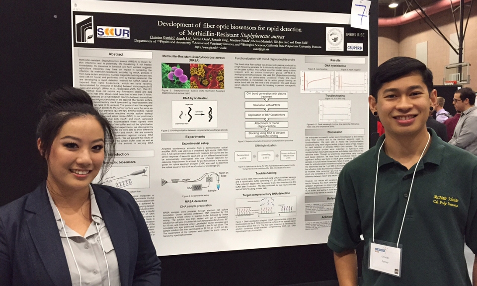 Two students pose in front of their poster presentation