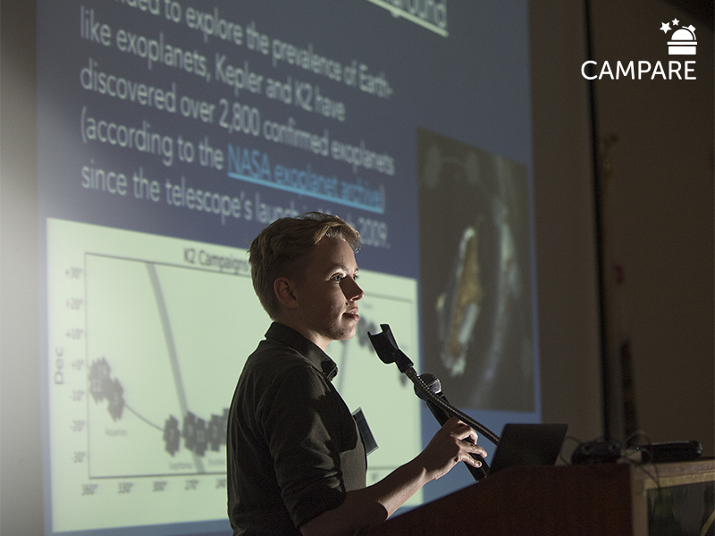 Student at podium with a projected presentation behind them and campare logo on upper right hand corner