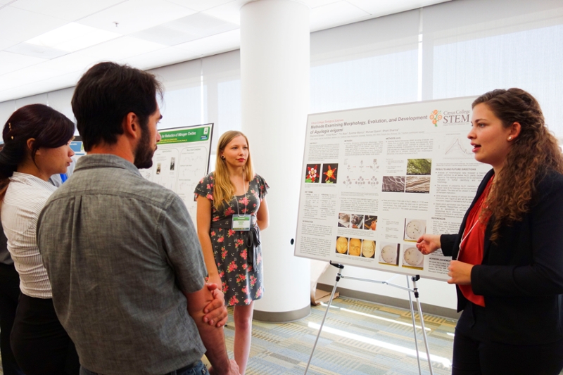 Two students standing in front of their poster presentation engaged in conversation with guests