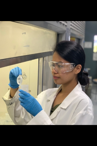 Student in a lab coat and gloves handling material in a lab