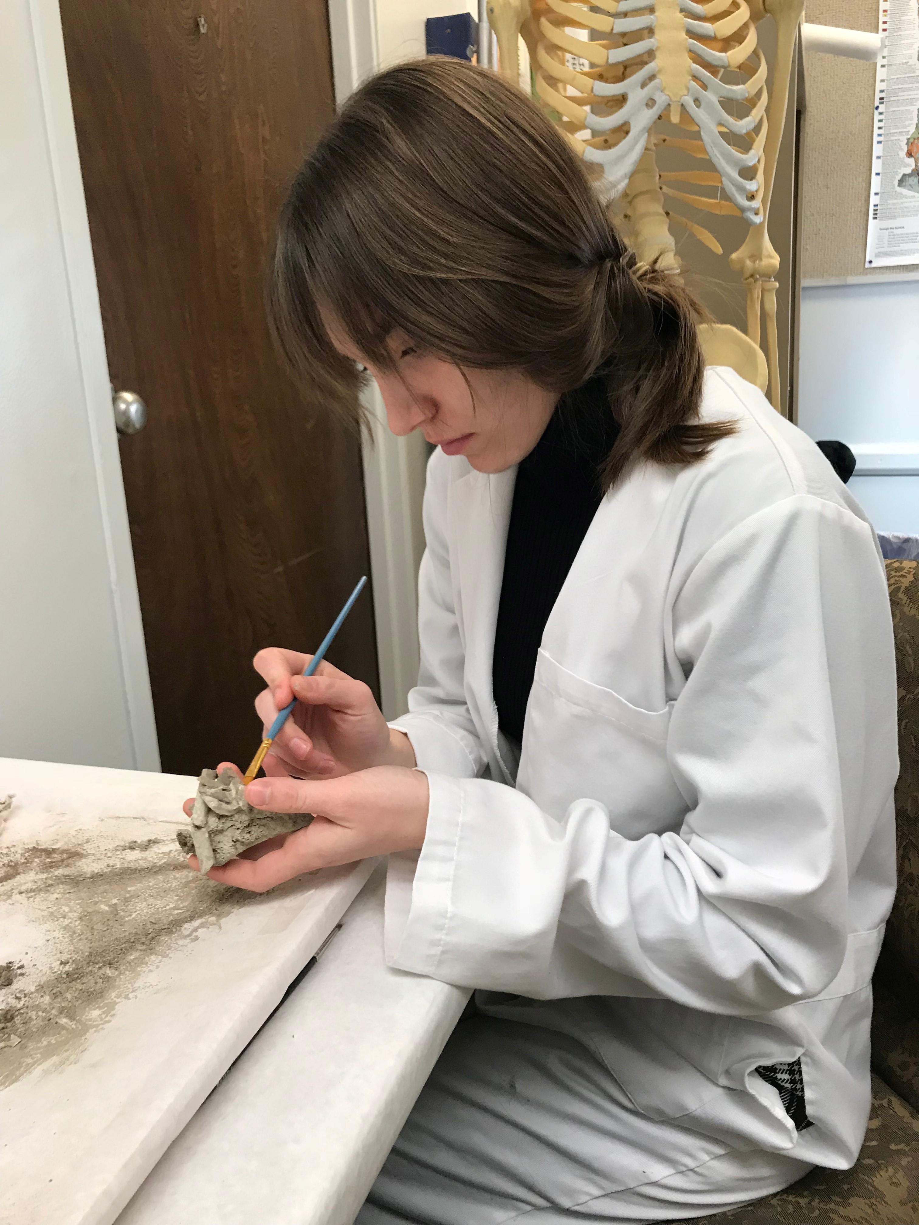 Student in a lab coat brushing an object