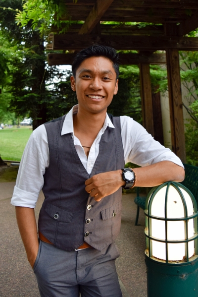 Male student in a suit confidently posing outdoors and resting his left hand on a light