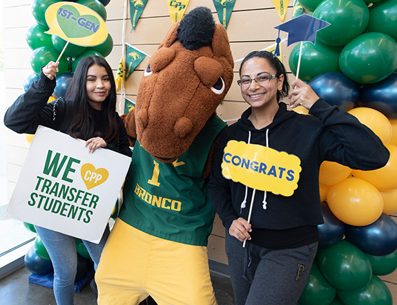 Image of two students holding transfer-themed props while surrounding a horse mascot