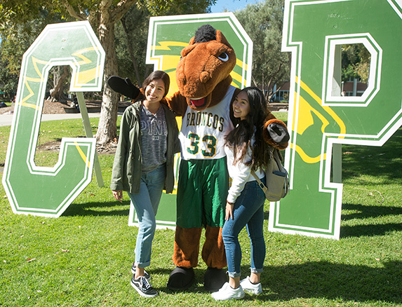 Two female students pose with Billy Bronco at CPP letters