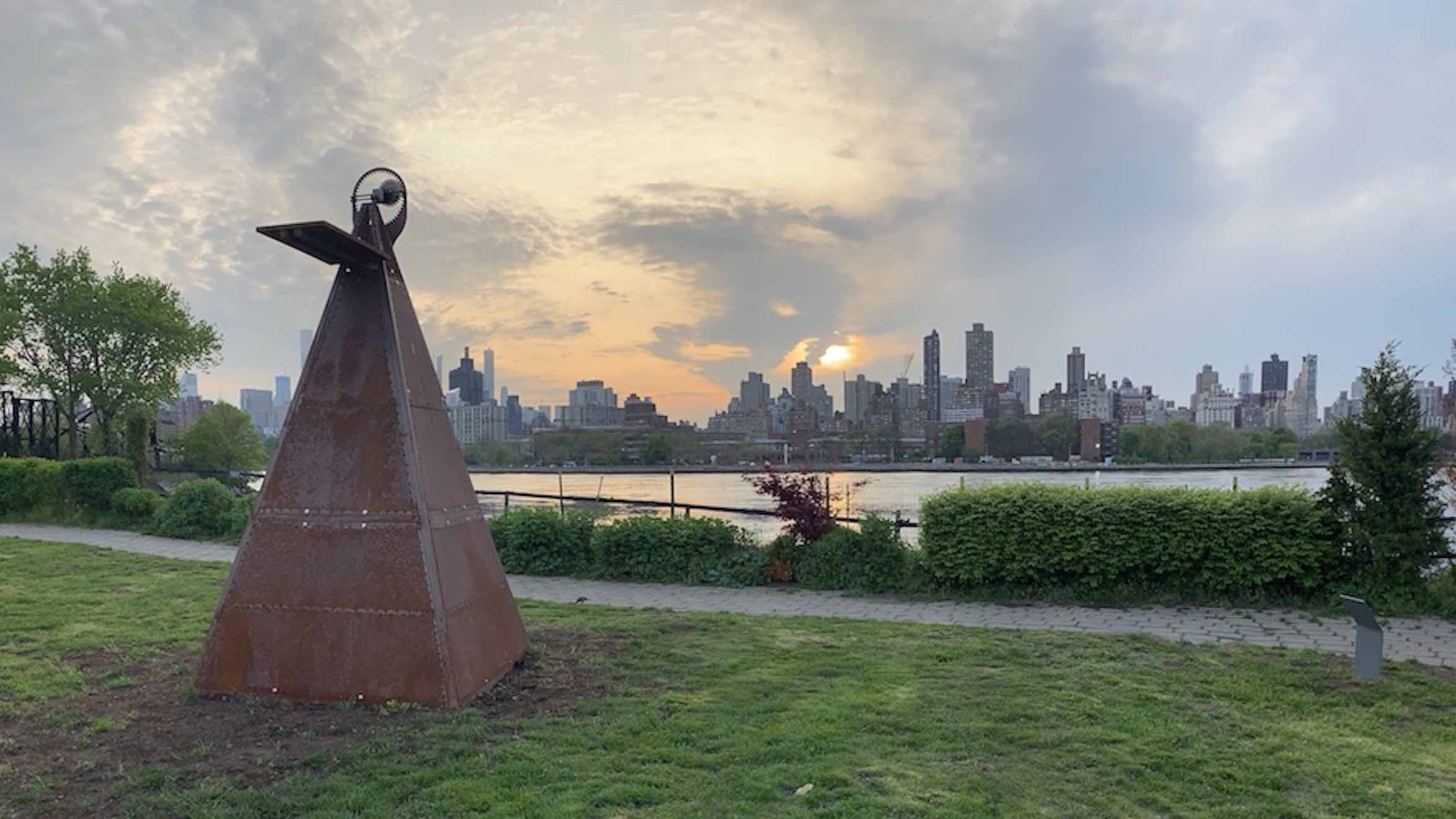 A long rusted pyramid structure placed near a park's walking path