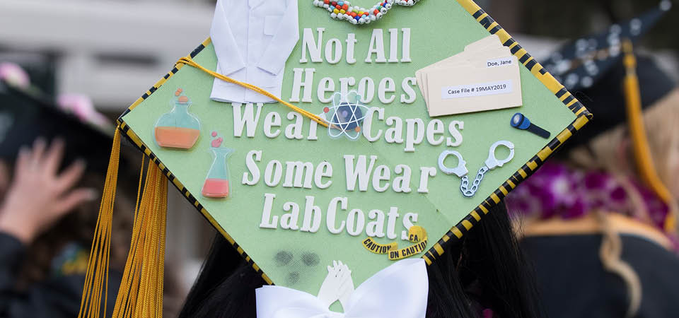 A student’s graduation cap that says 'Not all heroes wear capes, some wear lab coats.'