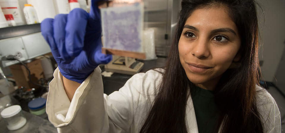A female student holds up a microscope plate to the camera