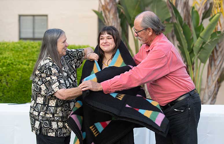 Two loved ones putting a native american blanket over their native grad