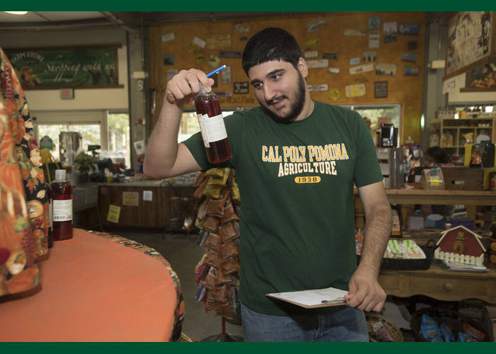 CPP Student holding a clipboard and inspecting a bottle inside the Farm Store.