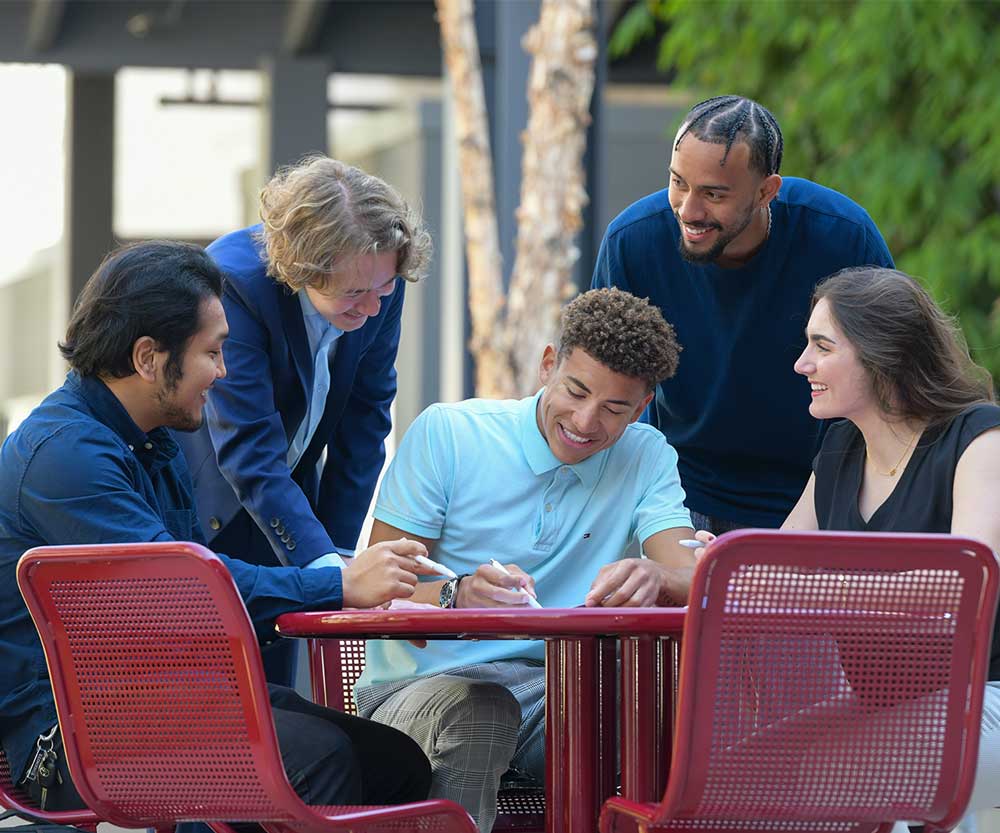Group of students in CBA courtyard sitting around a laptop