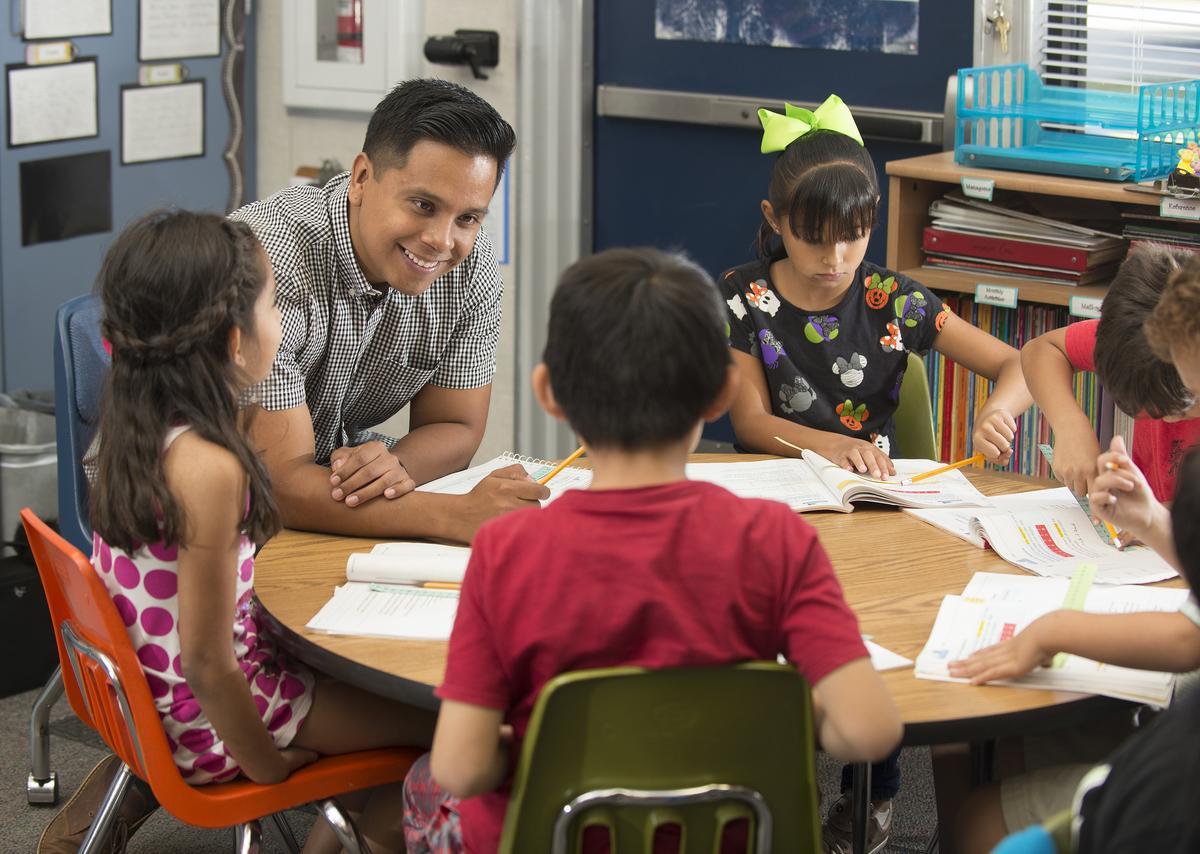 A alum smiles at a table with his students. 