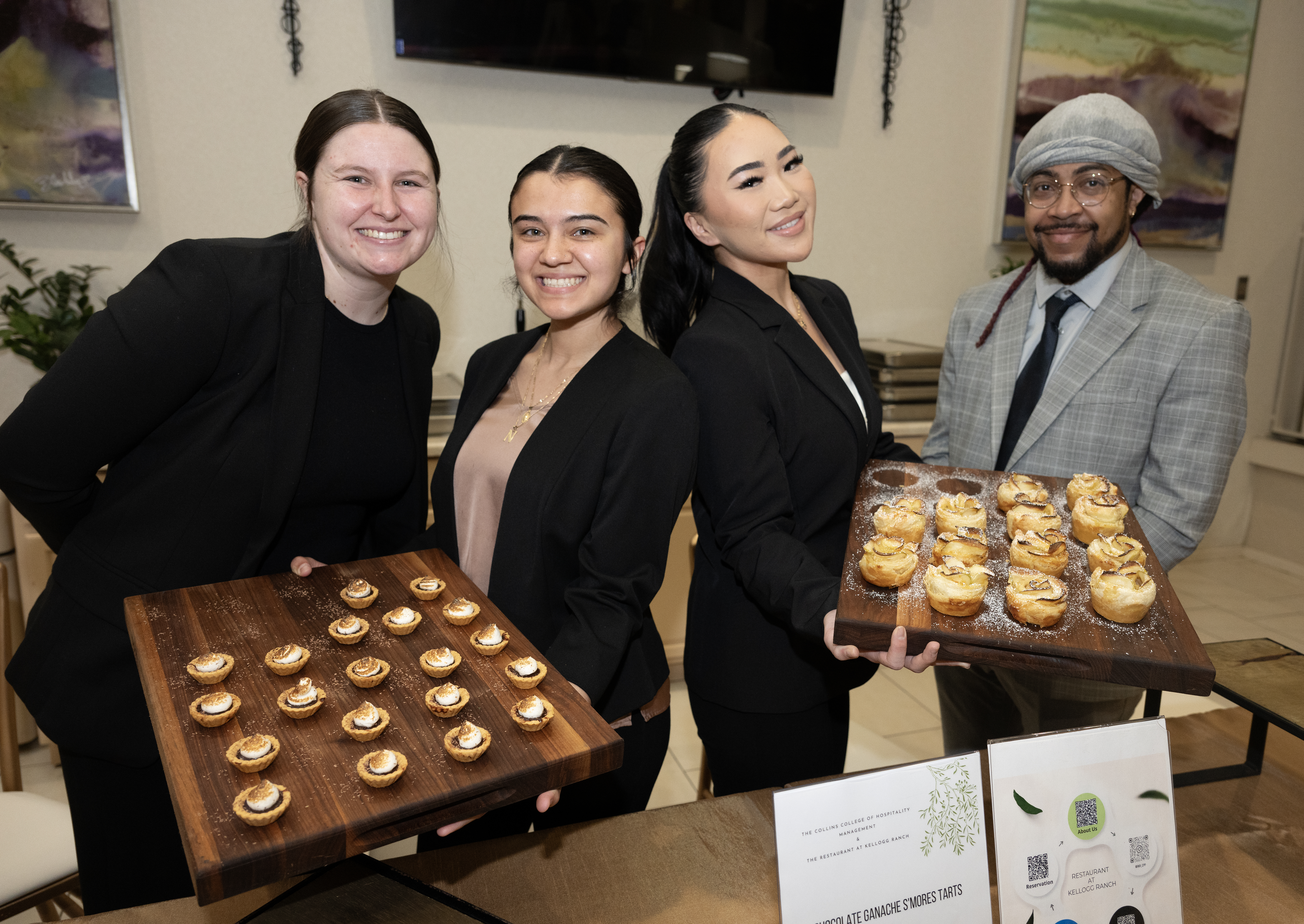 4 students paired holding a tray of baked desserts