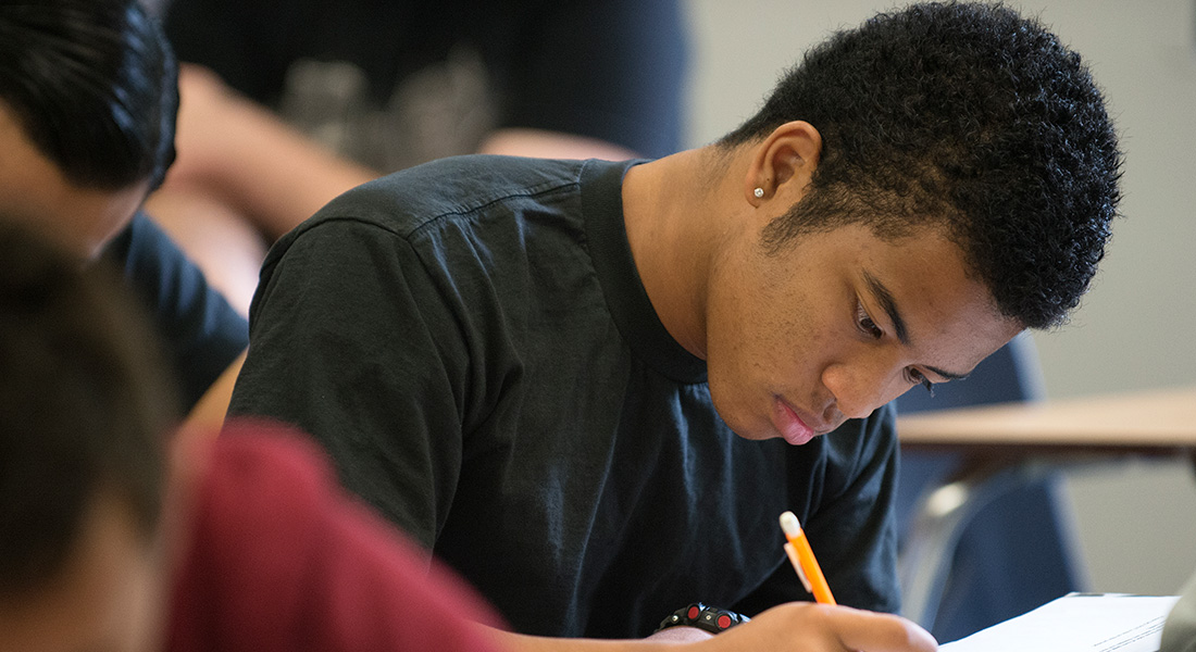 Male black student writing in a notebook during class