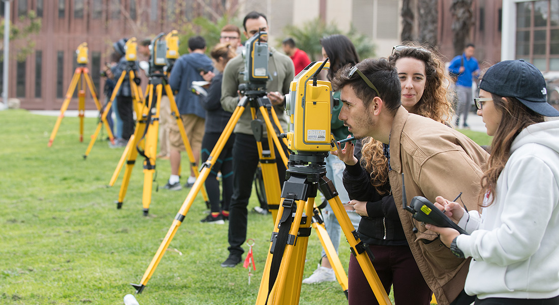 Advanced Surveying class outdoors looking through equipment.