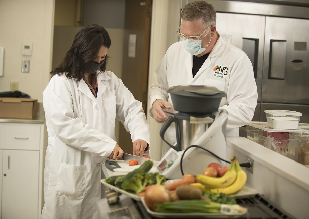 Female student and male professor cutting fruit and vegetables.