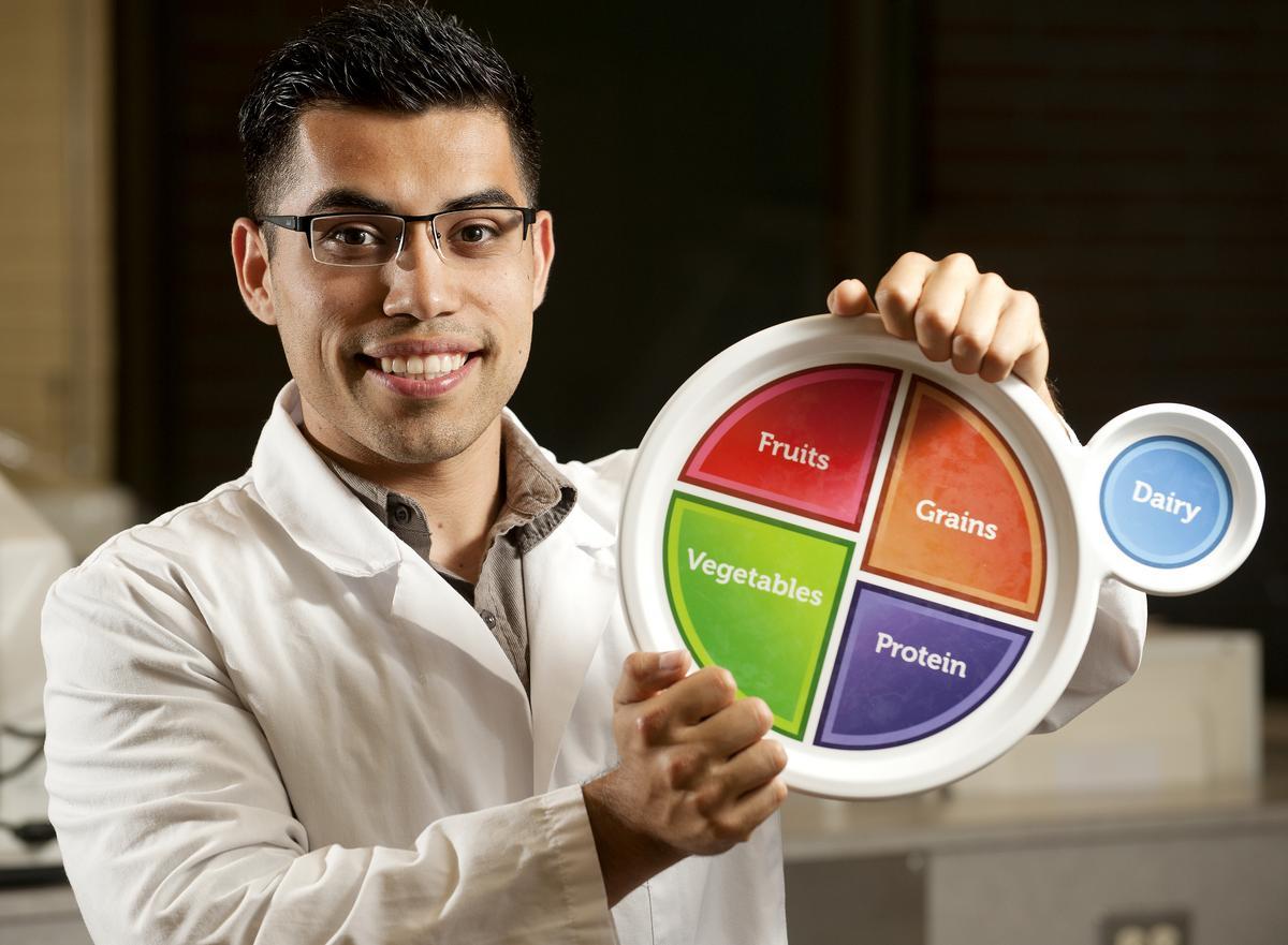 Male student holds a portion guide for fruits, vegetables, grains, proteins and dairy.