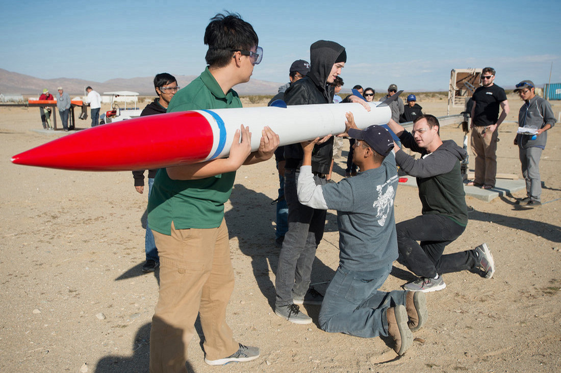 A group of students hold and prepare a rocket