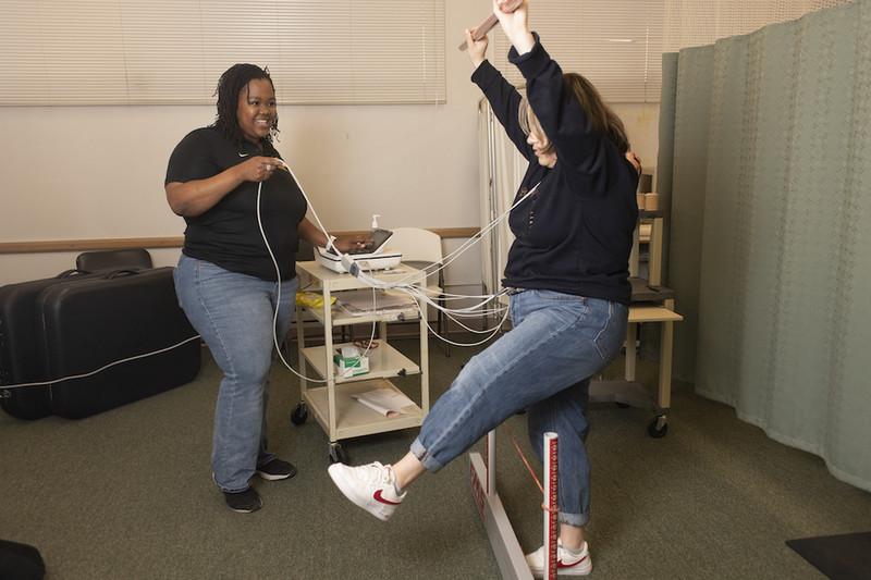 Kinesiology student balancing and hooked up to equipment while a professor watches