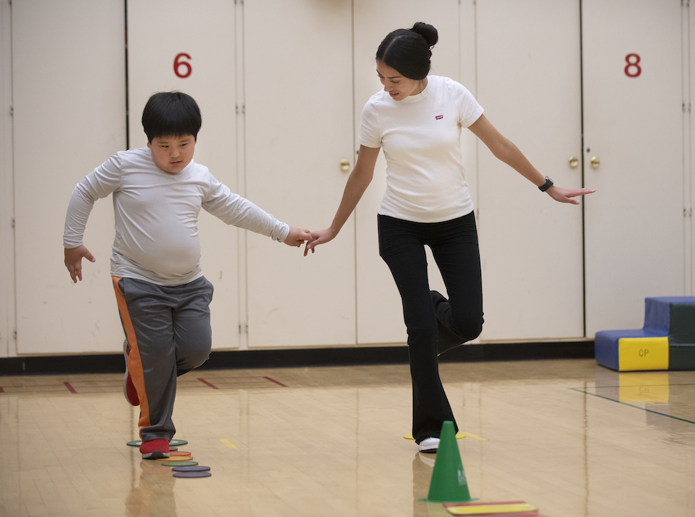 Kinesiology student helping a child balance on one foot