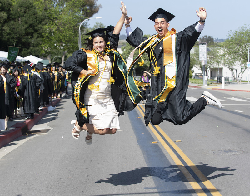 two graduates wearing caps and gowns jump in the air