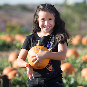 A girl smiles and holds a pumpkin