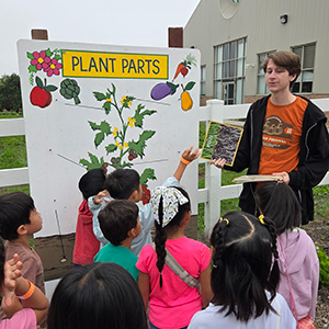 A male student teaches schoolchildren about plant parts.