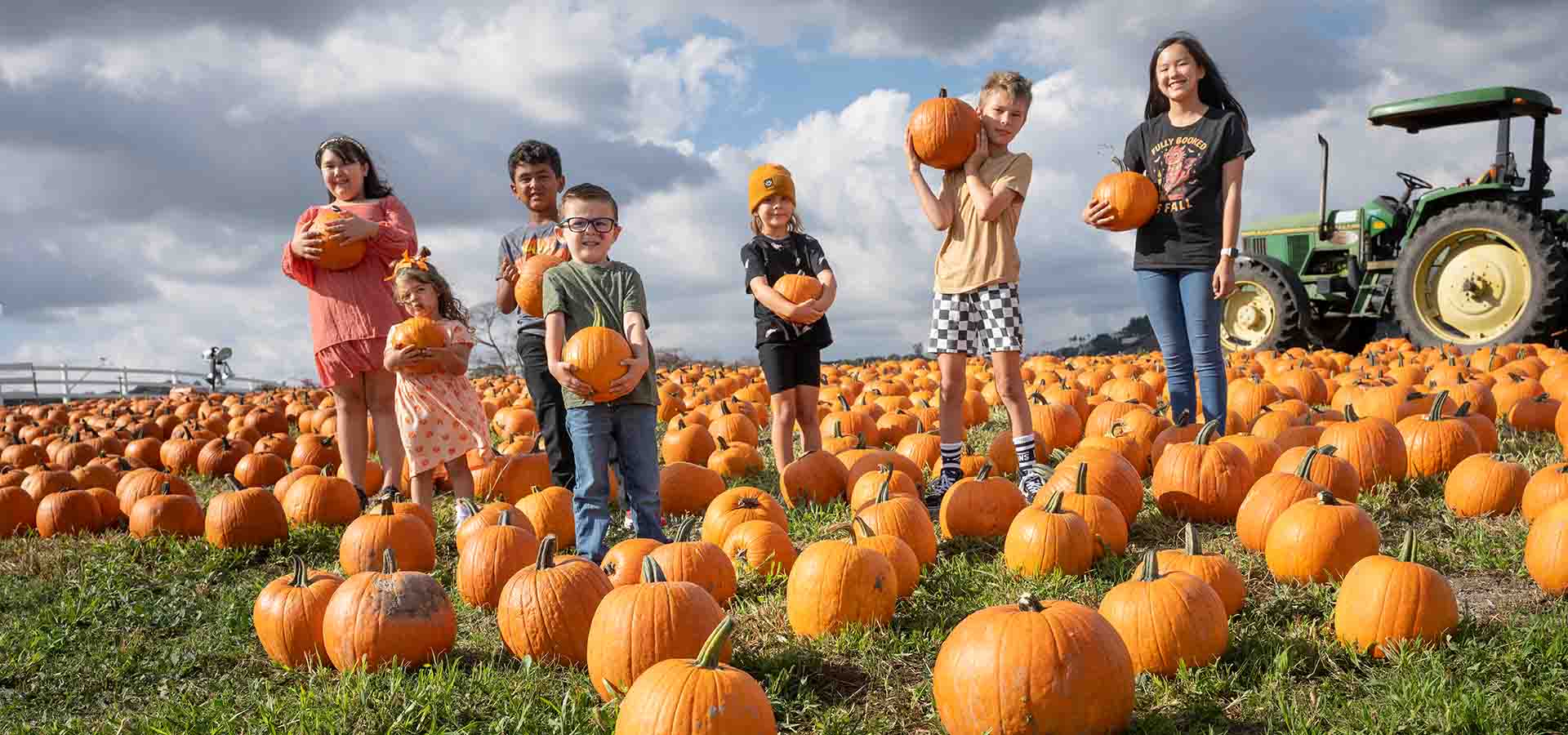 A group of kids holds pumpkins in the pumpkin patch