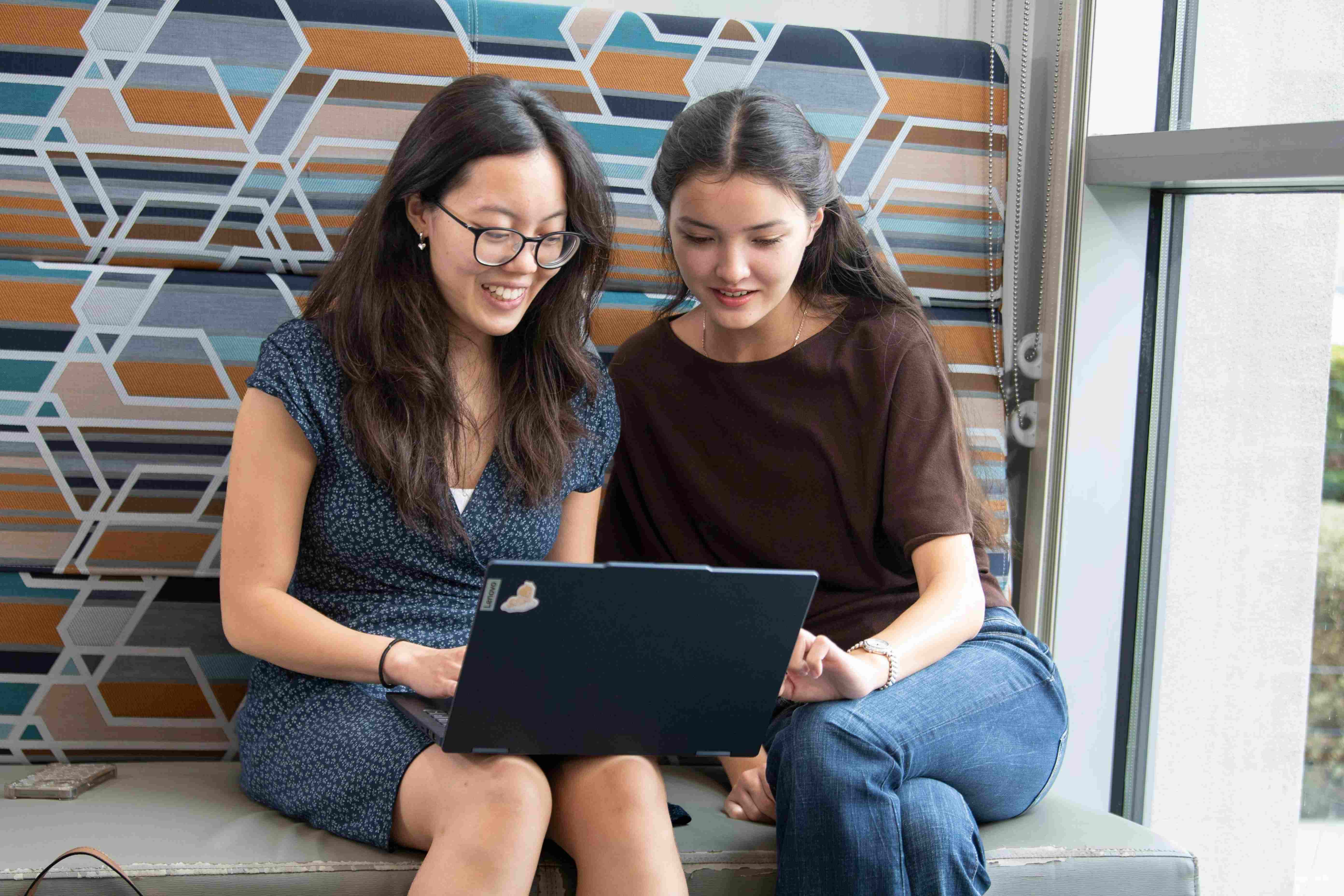 Two students using a laptop together sitting side by side