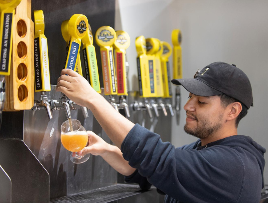 A student wearing a hat pouring beer on tap at Innovation Brew Works